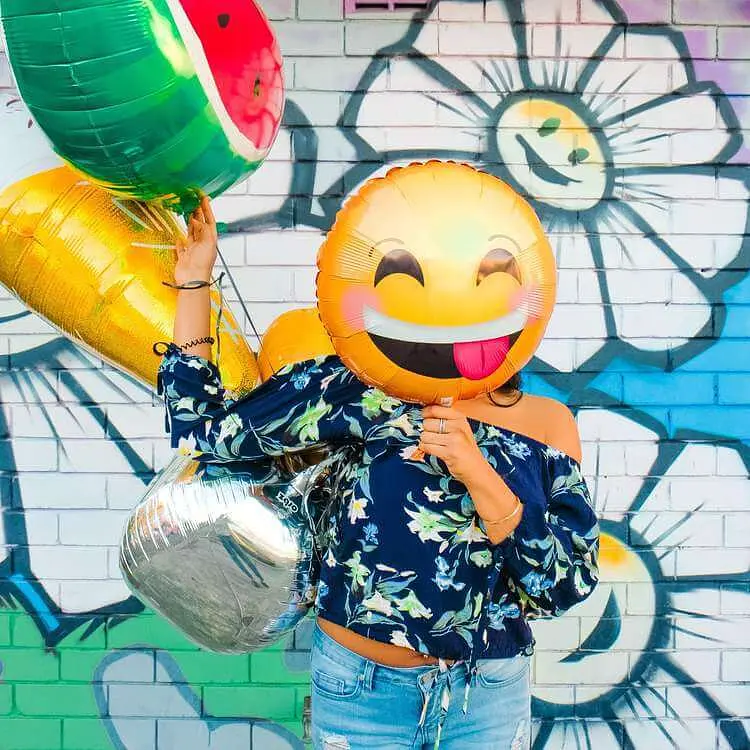 persoon met emoji ballonnen, smiley ballon voor haar gezicht