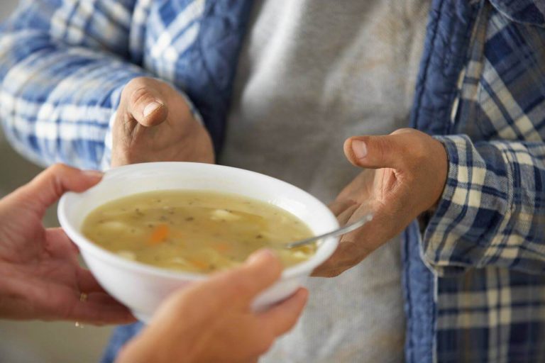 persoon dat een kom soep aan een andere persoon overhandigd