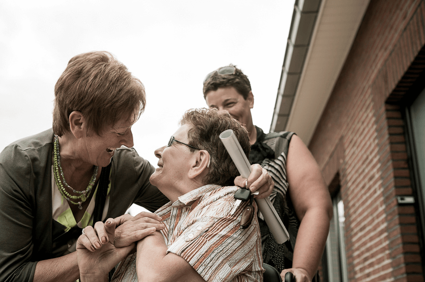 Two neighbors, one of whom in a wheelchair, hug each other.